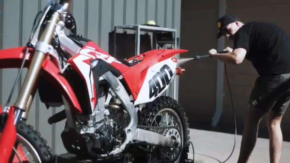 man cleaning dirt bike using water hose