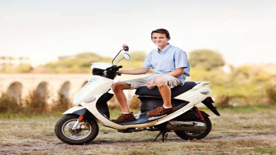 teen sitting on a moped parked along the road